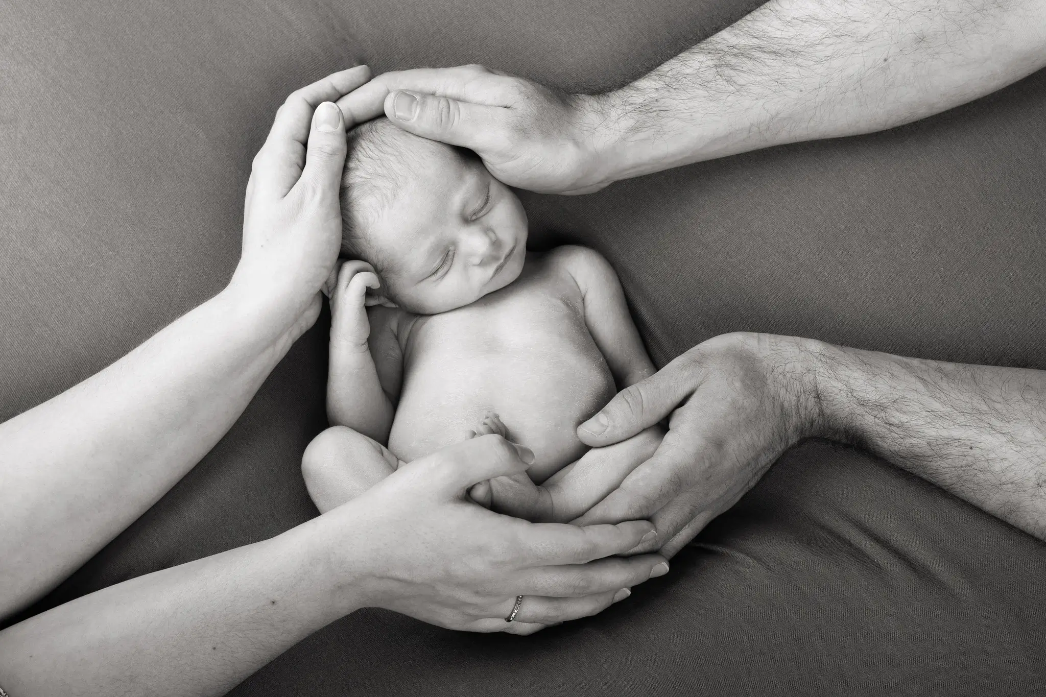 Photo noir et blanc bébé emmailloté dans les mains de ses parents par la photographe Julie Kirtz
