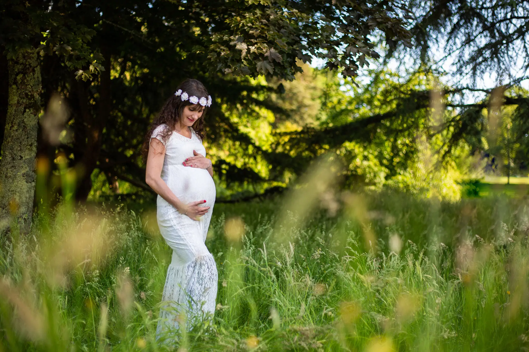 Photo de femme enceinte dans la nature en robre blanche avec une couronne de fleurs blanche