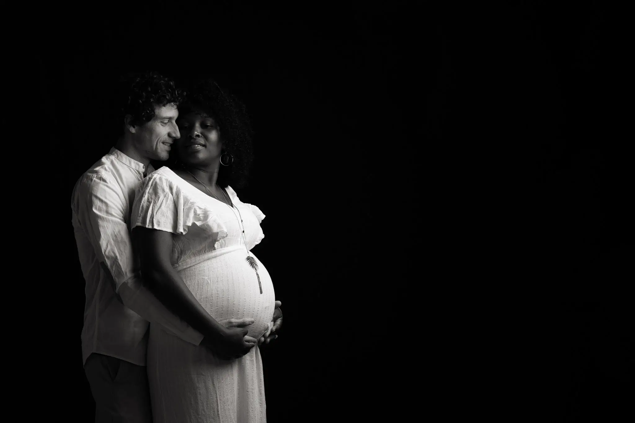 Photo de femme enceinte et future papa, en noir et blanc sur fond noir 