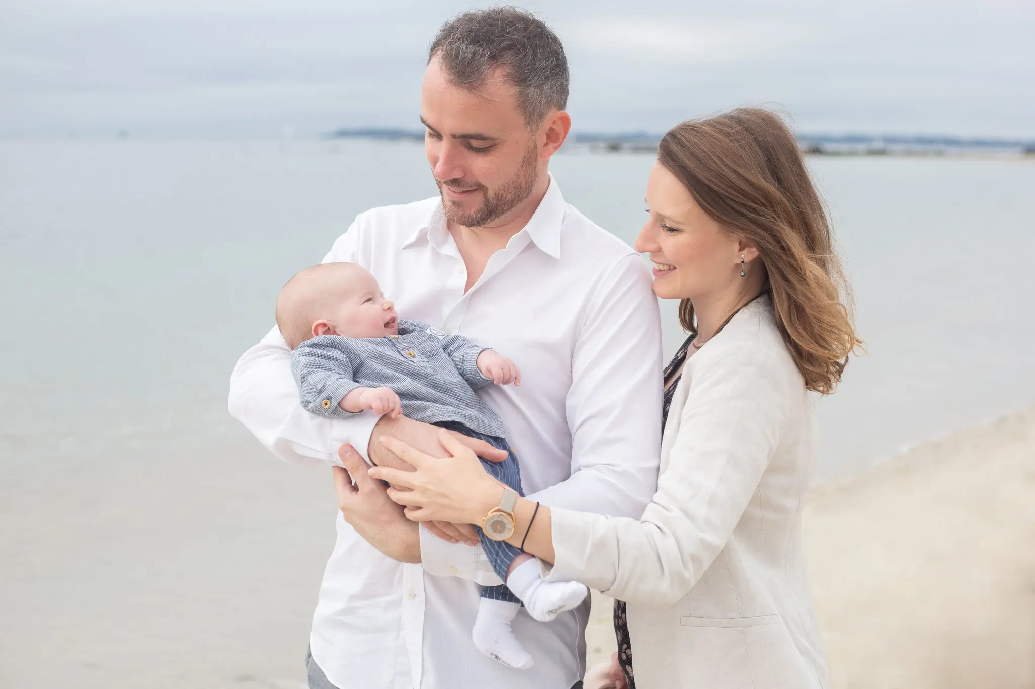 Séance couple avec bébé qui sourit sur la plage 