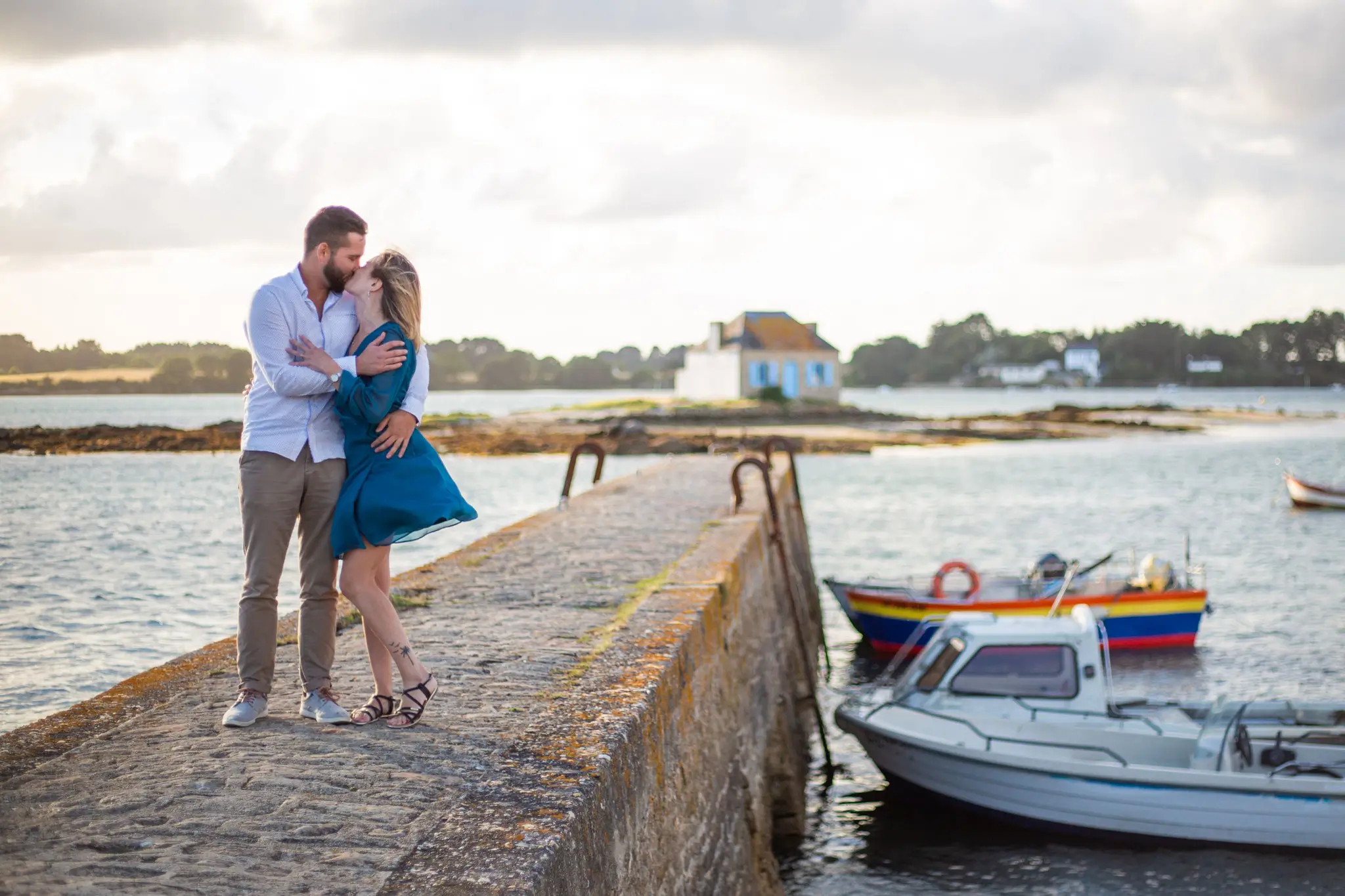 Photo de couple qui s'embrasse face à la mer et des bateaux